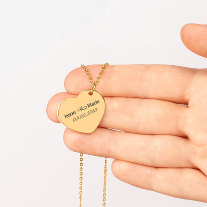 Gold plated heart pendant engraved with two names and a date, held in an open hand