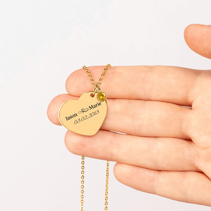 Gold plated heart pendant engraved with two names and a date, held in an open hand