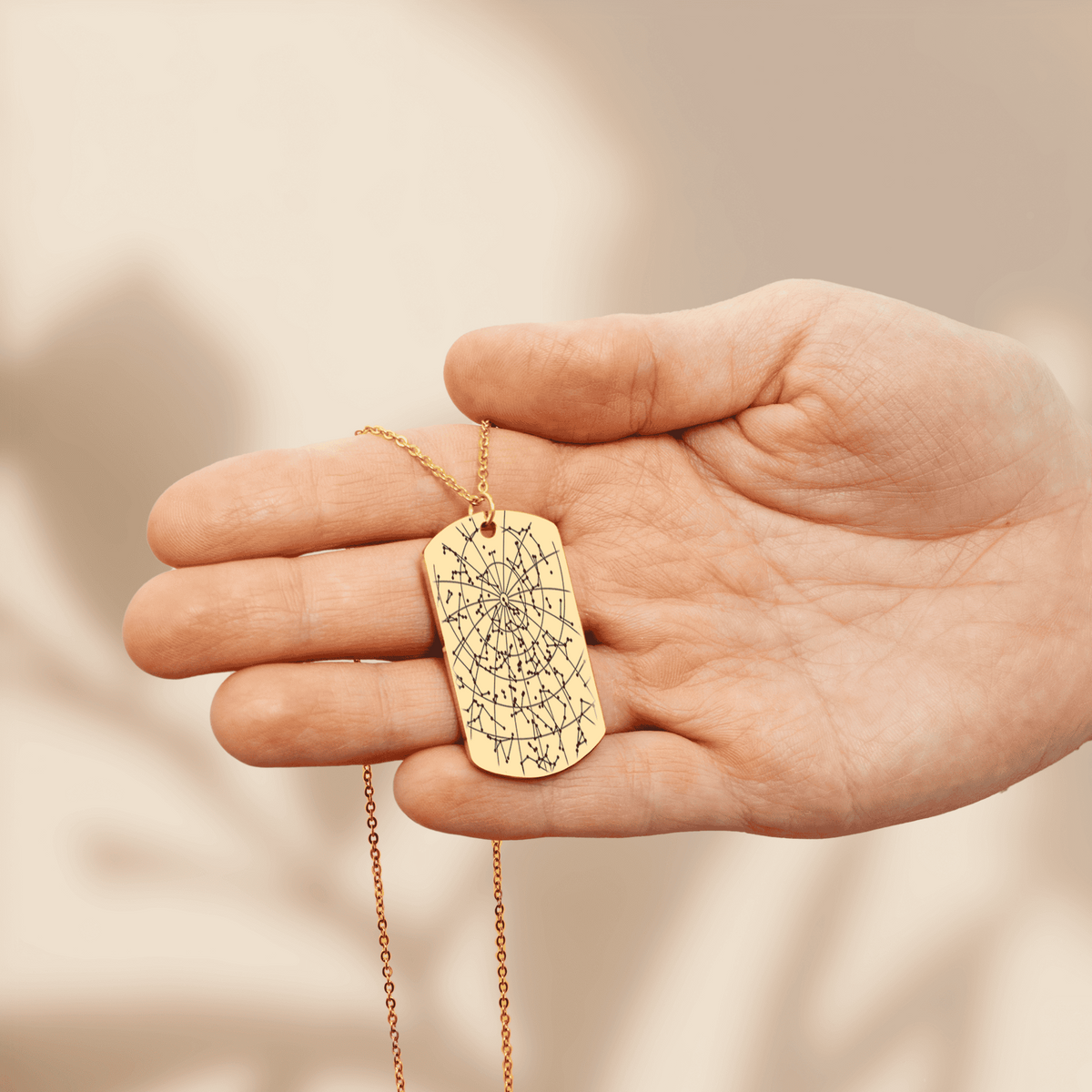 Gold plated star map tag pendant engraved with the night sky of a date and place, held in an open hand