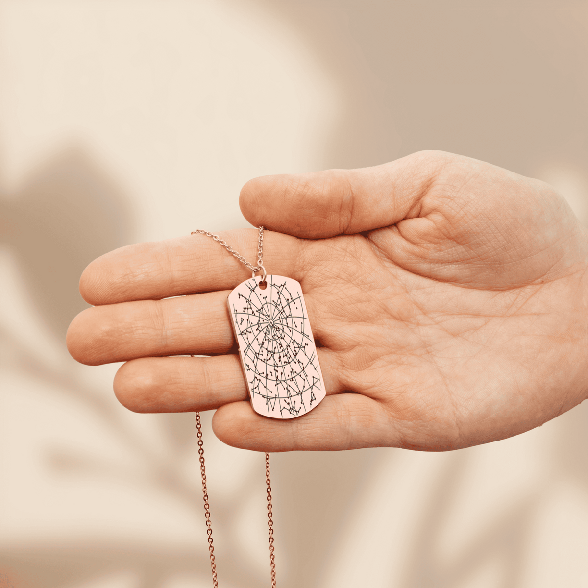 Rose gold plated star map tag pendant engraved with the night sky of a date and place, held in an open hand