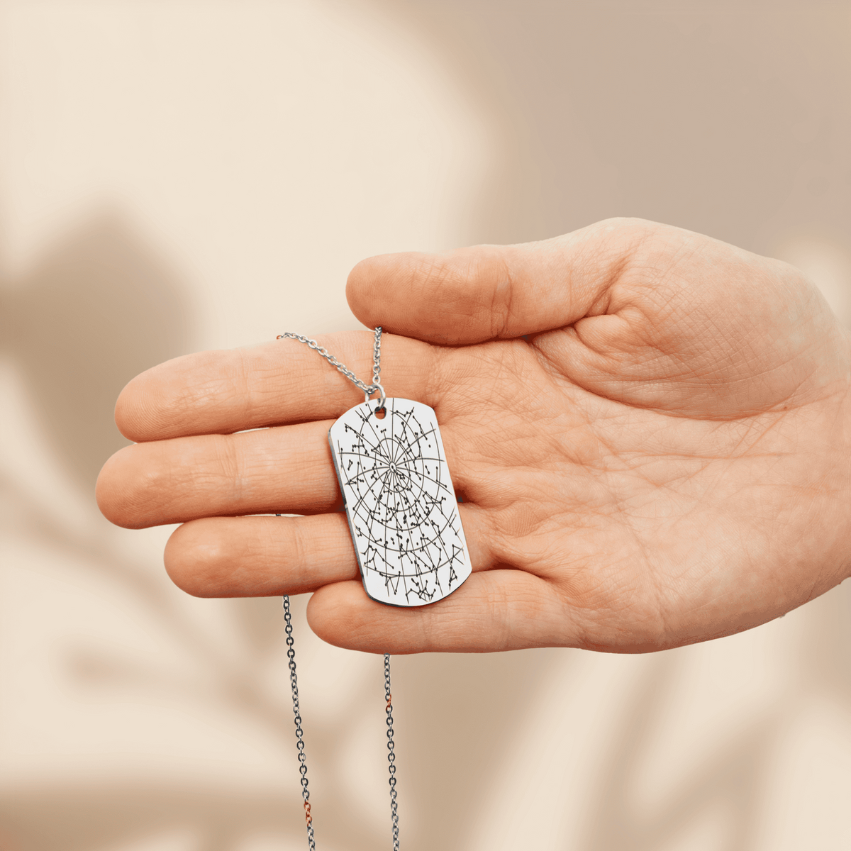 Stainless steel star map tag pendant engraved with the night sky of a date and place, held in an open hand