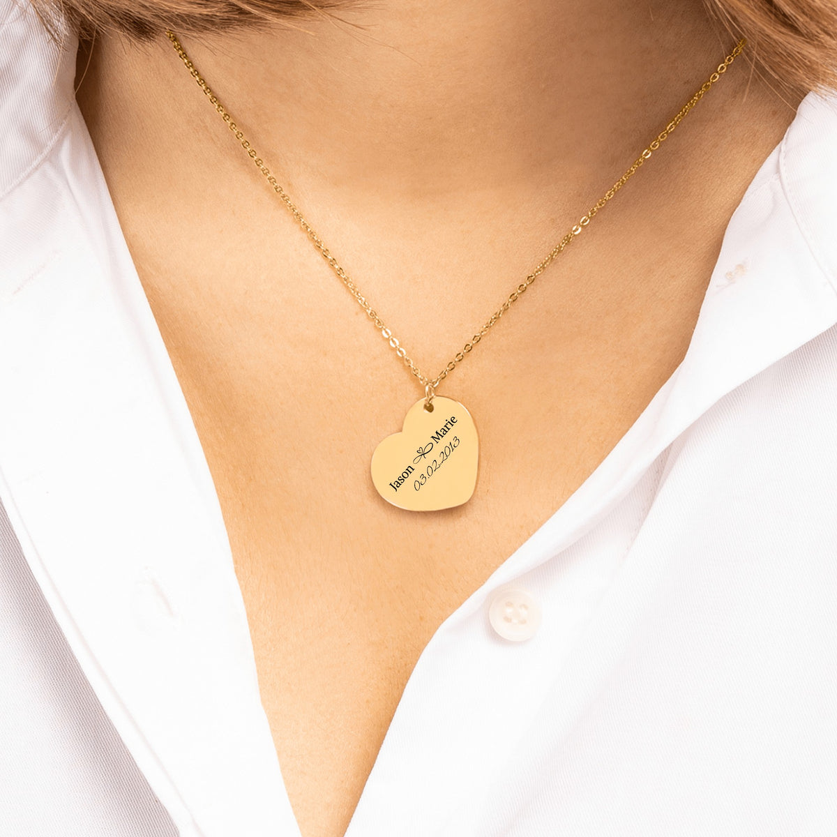 Gold heart pendant engraved with two names and a date, worn