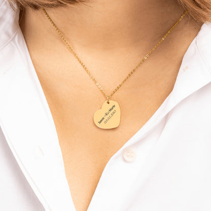 Gold heart pendant engraved with two names and a date, worn