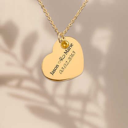 Gold plated heart pendant engraved with two names and a date, on a warm sand background