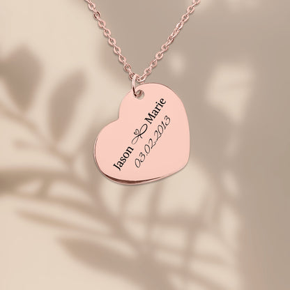 Rose gold plated heart pendant engraved with two names and a date, on a warm sand background