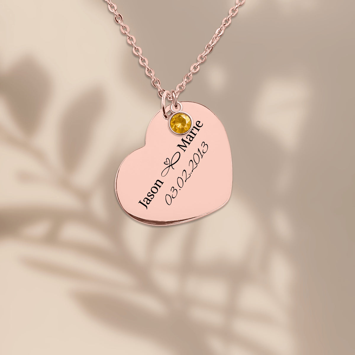 Rose gold plated heart pendant engraved with two names and a date, on a warm sand background