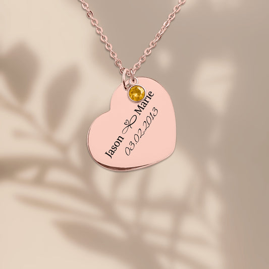 Rose gold plated heart pendant engraved with two names and a date, on a warm sand background